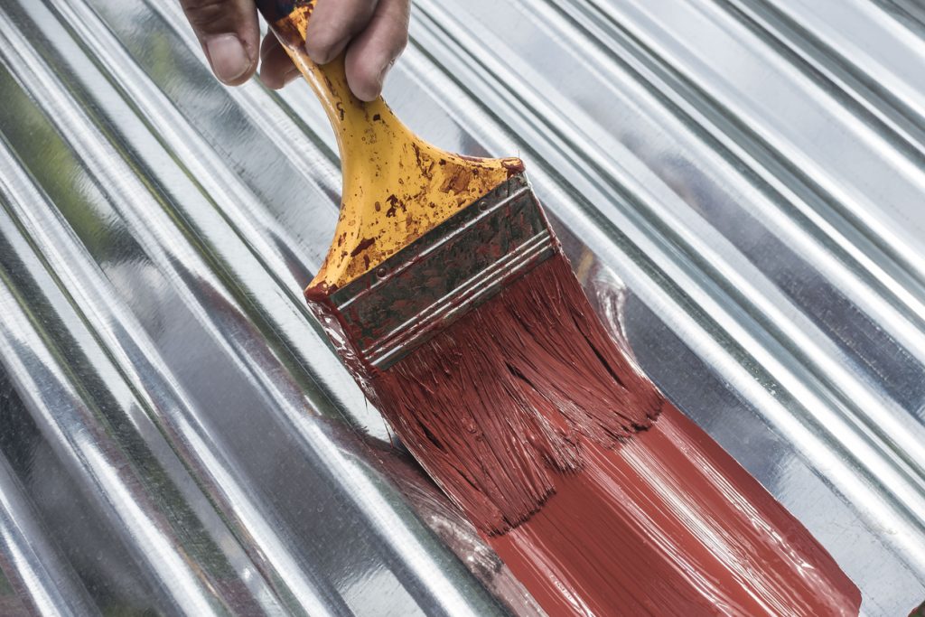 Painting the surface of a sheet of Galvanized Iron or GI corrugated metal with rust inhibiting red oxide primer.