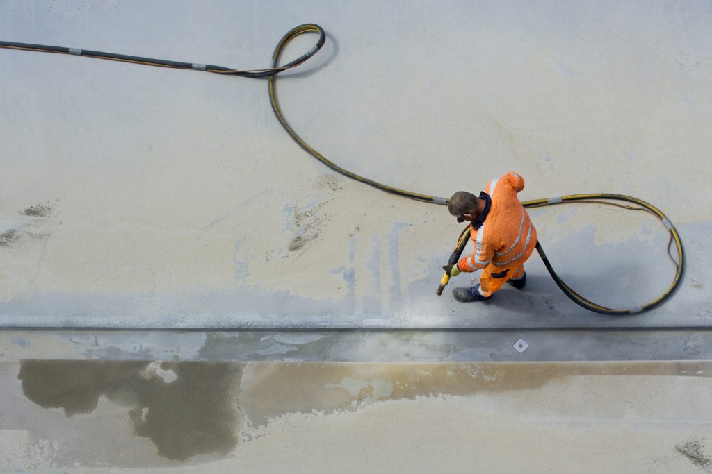 Man in orange sandblasting concrete surface with air pressure hose